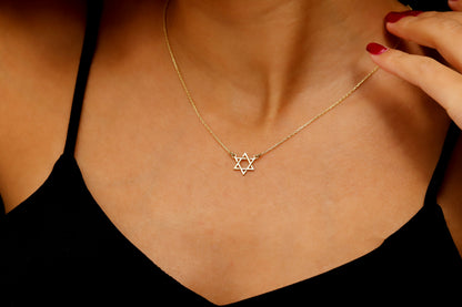 A close-up image of a person wearing a black tank top showcasing a gold Star of David necklace.