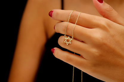 A close-up image of a person wearing a black tank top showcasing a gold Star of David necklace.