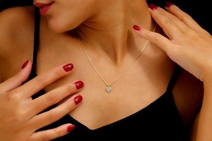 A close-up image of a woman wearing a 14K gold pave diamond heart necklace with a silver chain, showcased on a black dress.