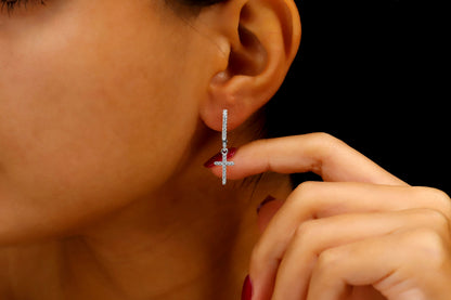 A close-up image of a woman's ear wearing a silver diamond cross dangle earring.