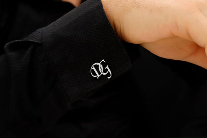 A close-up image of a man's hand holding a personalized cufflink with a monogram initial on it.
