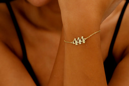 A close-up image of a person's wrist wearing a gold bracelet with 444  number sequence charm.