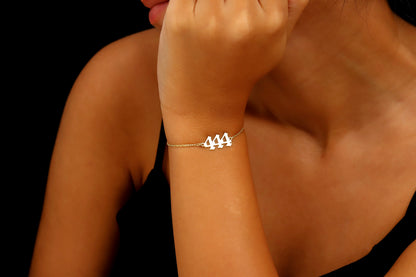 A close-up image of a person's wrist wearing a gold bracelet with 444  number sequence charm.
