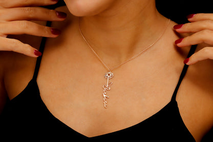 A woman wearing a black tank top showcasing a gold-filled vertical name necklace with floral designs.