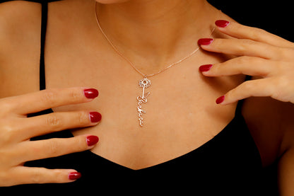 A woman wearing a black tank top showcasing a gold-filled vertical name necklace with floral designs.