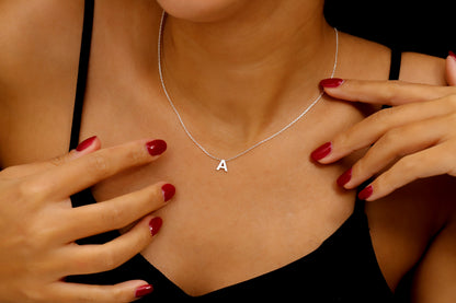 A person wearing a thin silver necklace with a small, minimalist "A" initial charm. A product by SilverGoldandRose.com.
