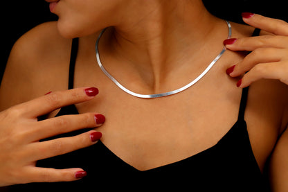 Silver necklace being worn by a person with red nail polish on a dark background