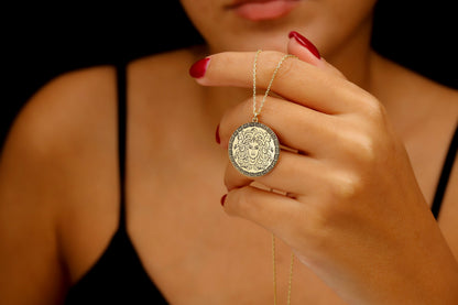 A close-up image of a person's fingers holding a silver necklace with a circular pendant featuring a design.