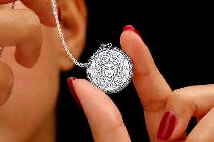A close-up image of a person's fingers holding a silver necklace with a circular pendant featuring a design.