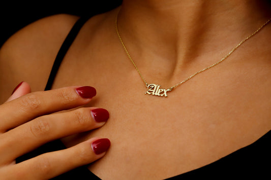 A close-up image of a woman wearing a gold-filled nameplate necklace with the name 'Alex' written in Old English font on a chain.