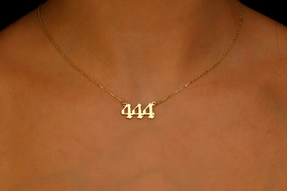 A close-up image of a necklace with the number 444 on a charm, held by a person with red nail polish.