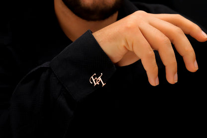 A close-up image of a man's hand holding a personalized cufflink with a monogram initial on it.