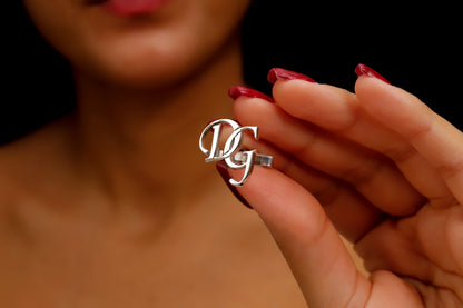 A close-up image of a man's hand holding a personalized cufflink with a monogram initial on it.