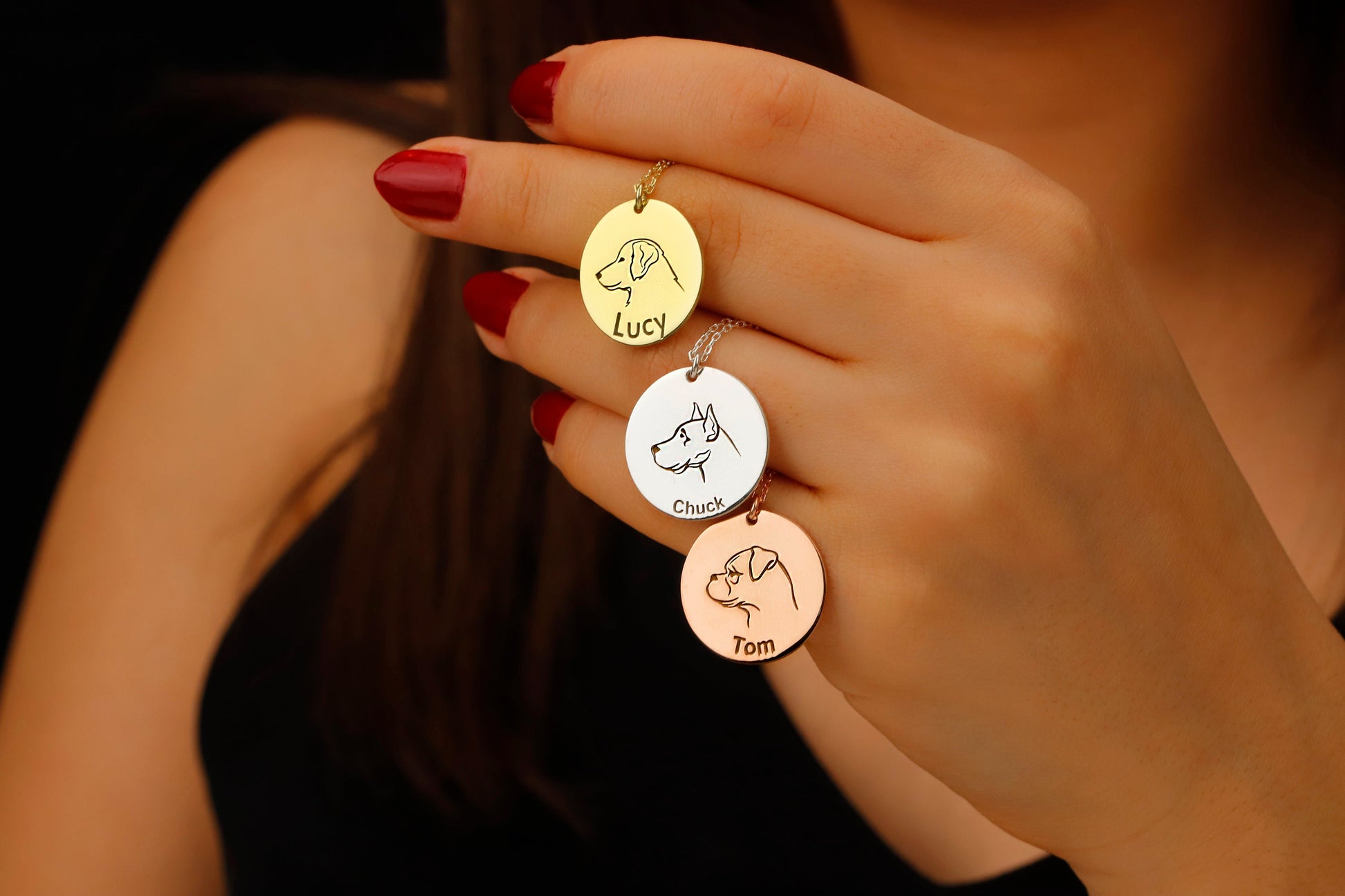 Hand holding three gold pendants with engraved names and dog illustrations.