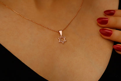 Rose gold necklace with Star of David pendant on a person's neck, hand with red nails visible.