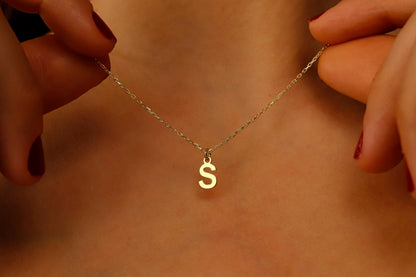 A close-up image of a person wearing a gold initial necklace with the letter 'S'.