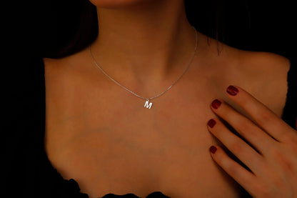 A close-up image of a person wearing a silver gold initial necklace with the letter 'M'.