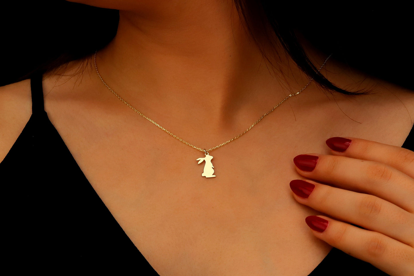 Gold necklace with a pendant worn by a person, with a hand touching the chest.