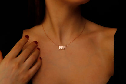 A close-up image of a necklace with the number '666' on a charm, held by a person with red nail polish.