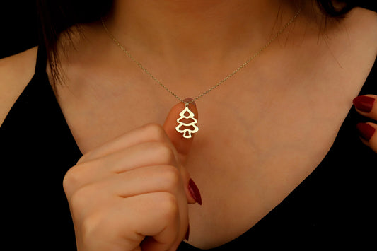 Gold necklace with a tree pendant worn by a person against a dark background