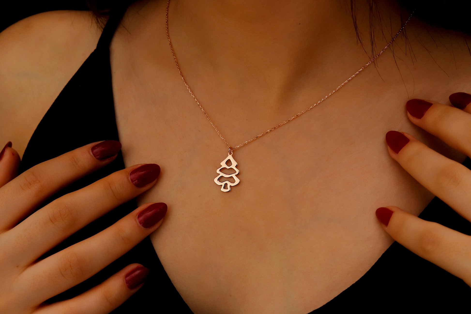 Rose gold necklace with a tree pendant worn by a person with red nail polish.