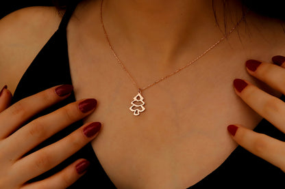Rose gold necklace with a tree pendant worn by a person with red nail polish.