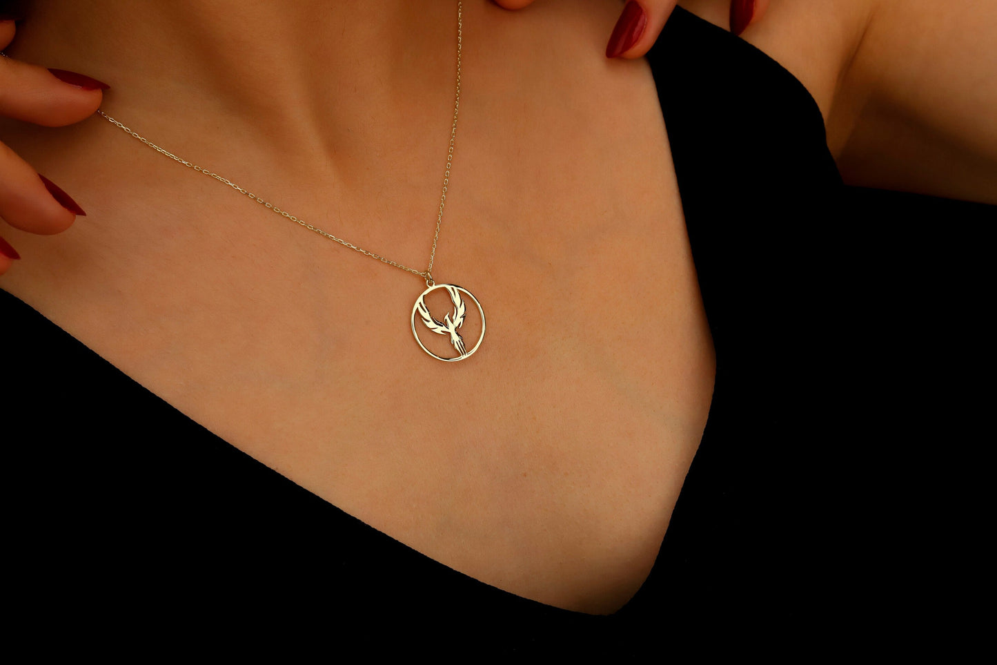 Gold necklace with a deer pendant on a person wearing a black top.