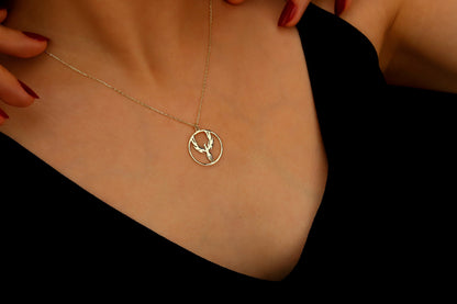 Gold necklace with a deer pendant on a person wearing a black top.