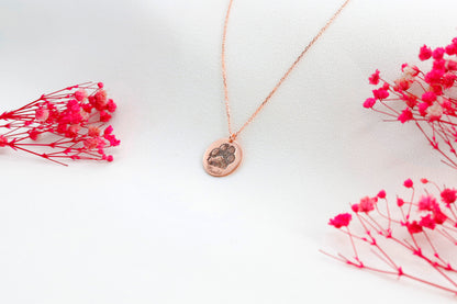 A rose gold-filled paw print necklace on a white surface, with a drawing of a paw print.