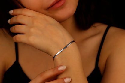 A close-up image of a woman's wrist wearing a silver flat snake chain bracelet.