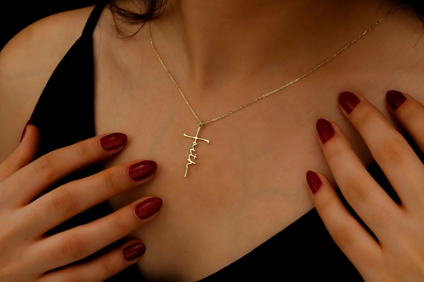 Gold necklace with a cross pendant on a person's chest, with hands touching the neckline.