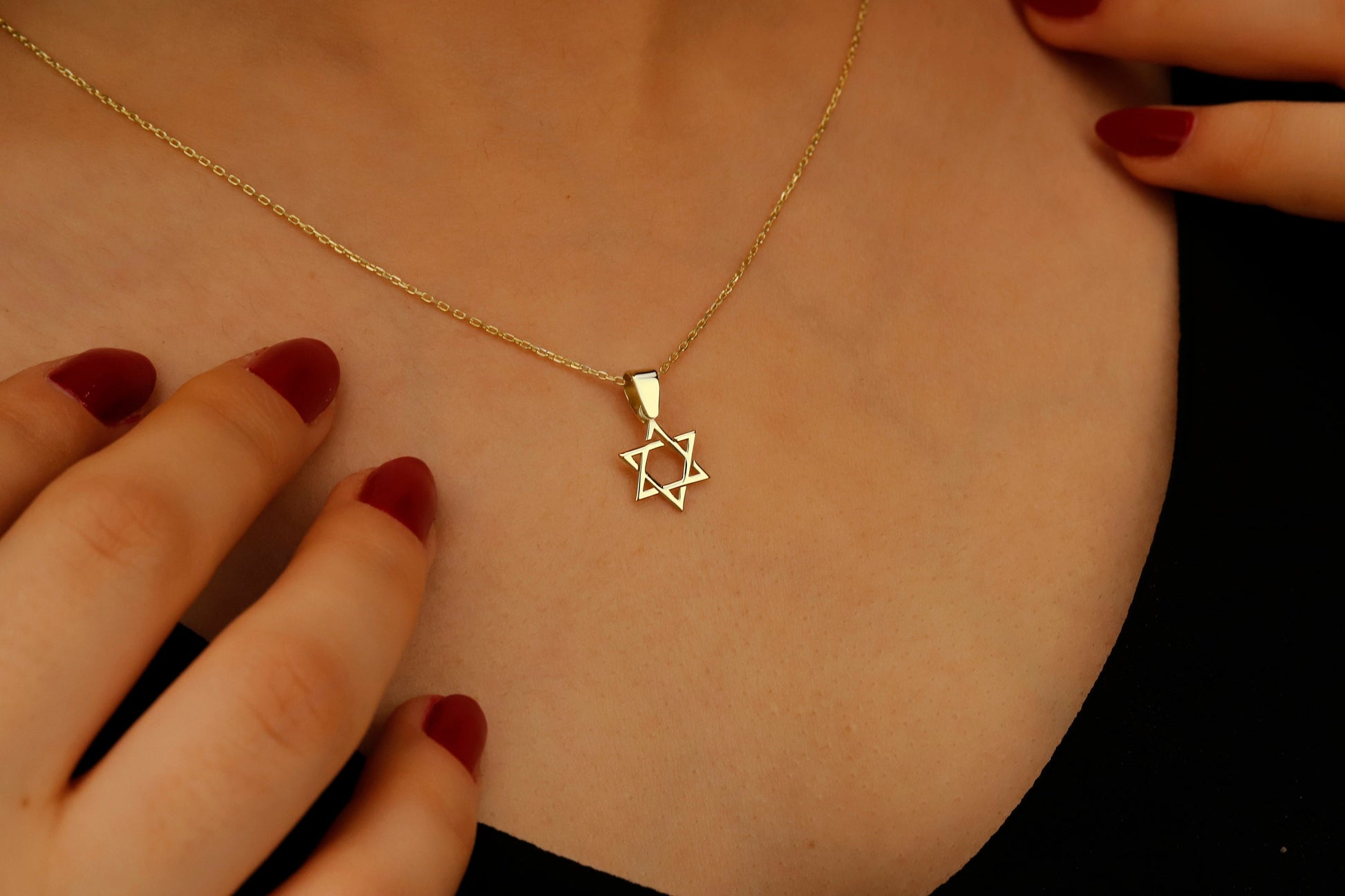 Gold necklace with a Star of David pendant on a person's neck.