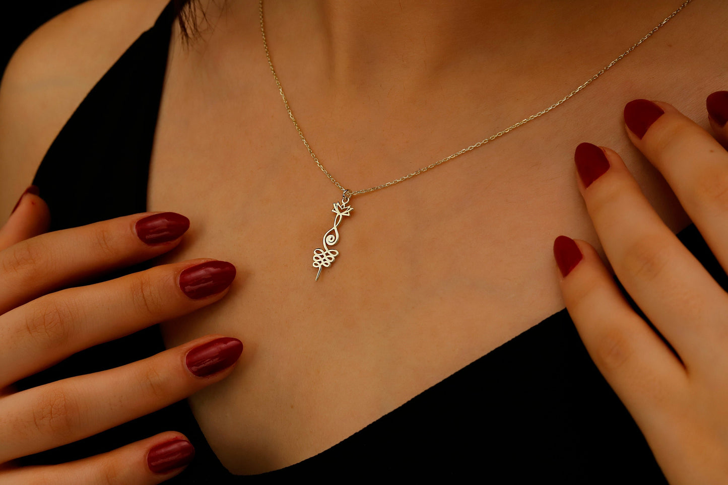 Necklace with a pendant worn by a person with red nail polish on their hands.