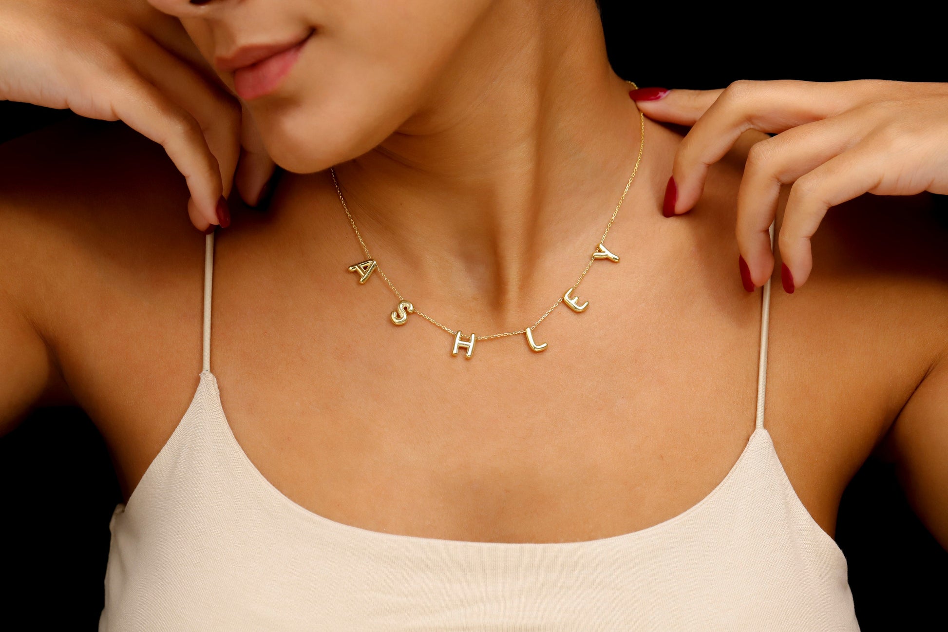 Woman wearing a gold necklace with 'ASHLEY' spelled out, against a black background
