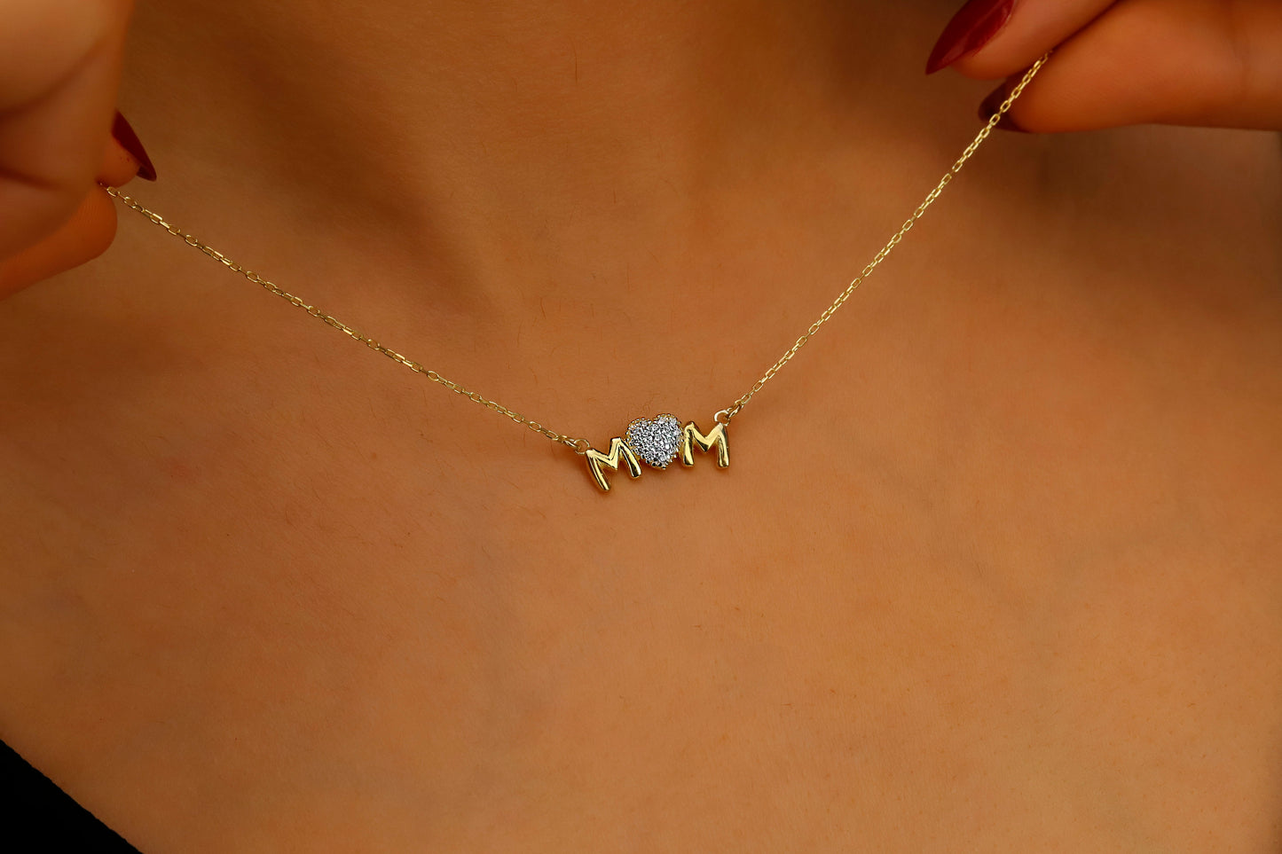 Gold necklace with 'MOM' pendant held against a beige background