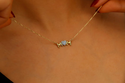 Gold necklace with 'MOM' pendant held against a beige background