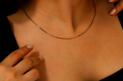 A close-up image of a gold box chain necklace with delicate layered chains, displayed on a person's neck.