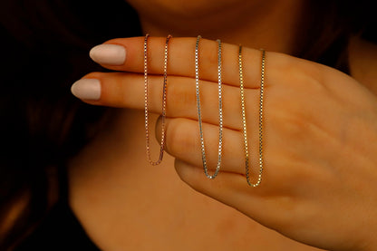A close-up image of 3 box chains necklace in gold silver and rose, displayed on a person's hand.