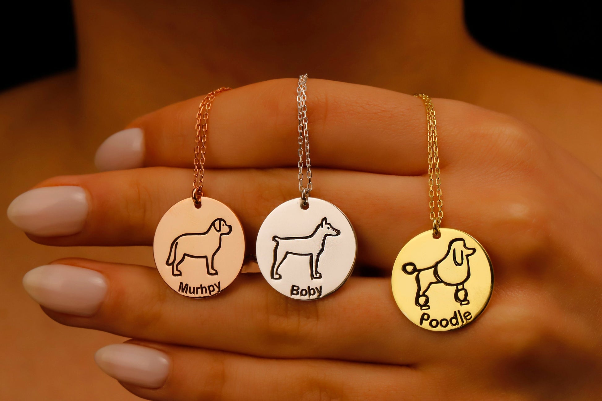 Three dog-themed necklaces with engraved names on a person's hand.