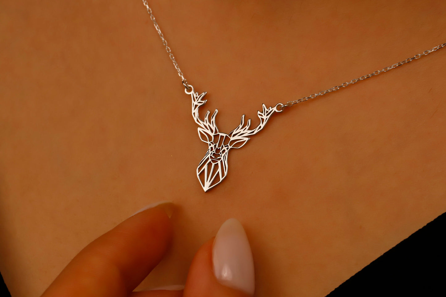 Silver deer-shaped necklace on a beige background