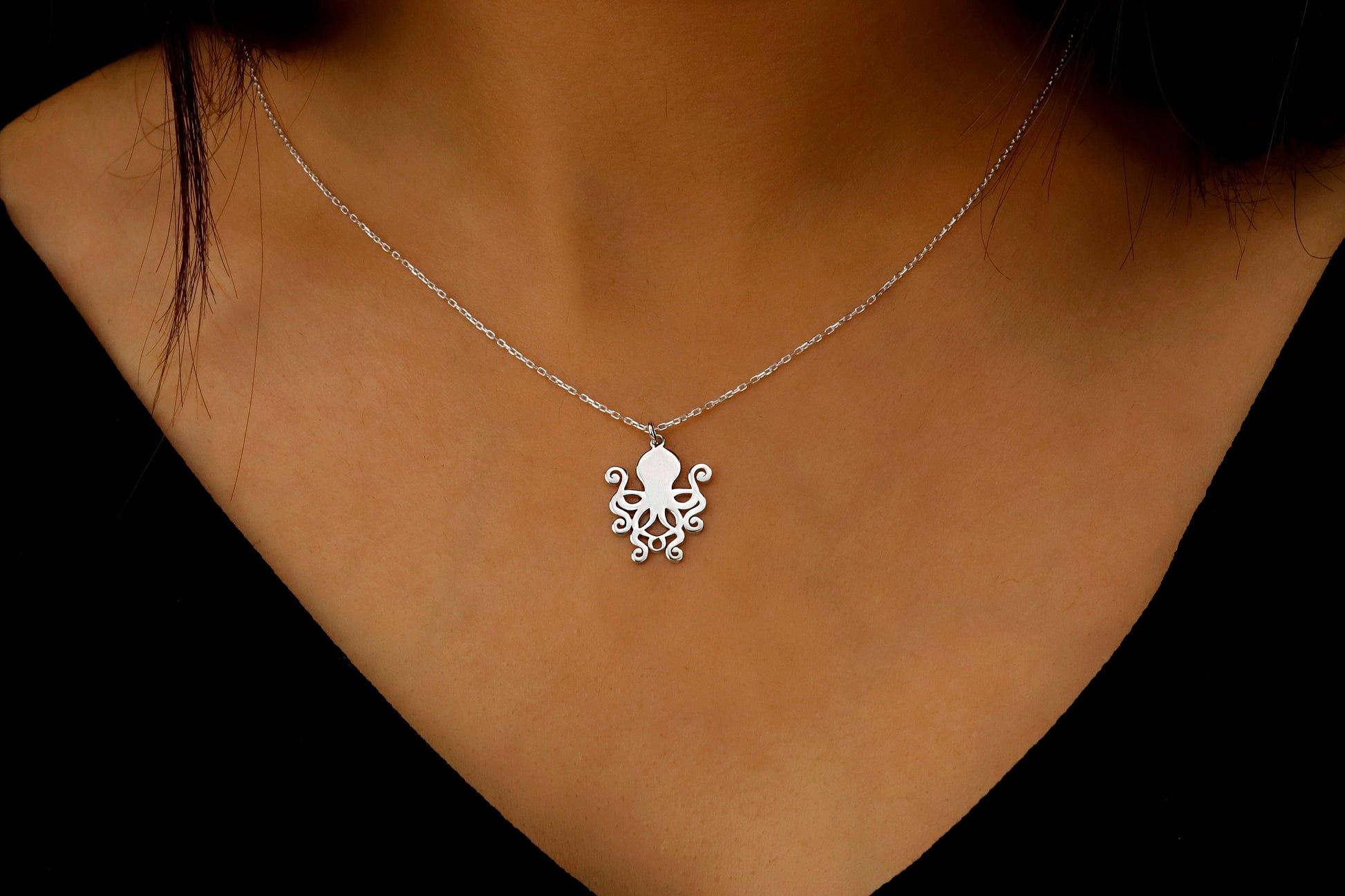 Silver octopus pendant necklace on a person's neck against a dark background