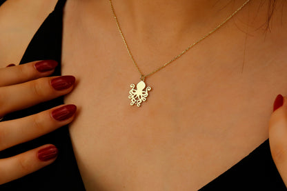Gold octopus necklace worn by a person with red nail polish on their fingers.