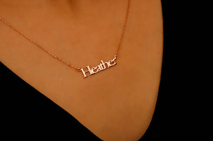 Gold necklace with 'Heather' pendant on a person's neck against a black background
