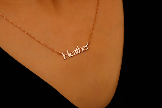 Gold necklace with 'Heather' pendant on a person's neck against a black background