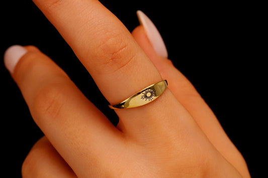 A minimalistic gold ring with a sunburst design on a black background.
