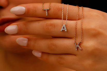 Three gold necklaces with 'T', 'A', and 'X' charms on a hand.