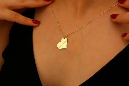 Gold heart-shaped necklace with engraved text on a person's neck
