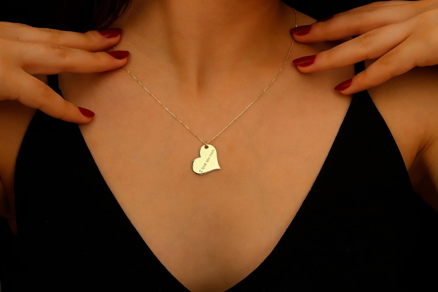 Gold necklace with a heart-shaped pendant worn by a person against a dark background