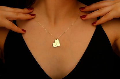 Gold necklace with a heart-shaped pendant worn by a person against a dark background