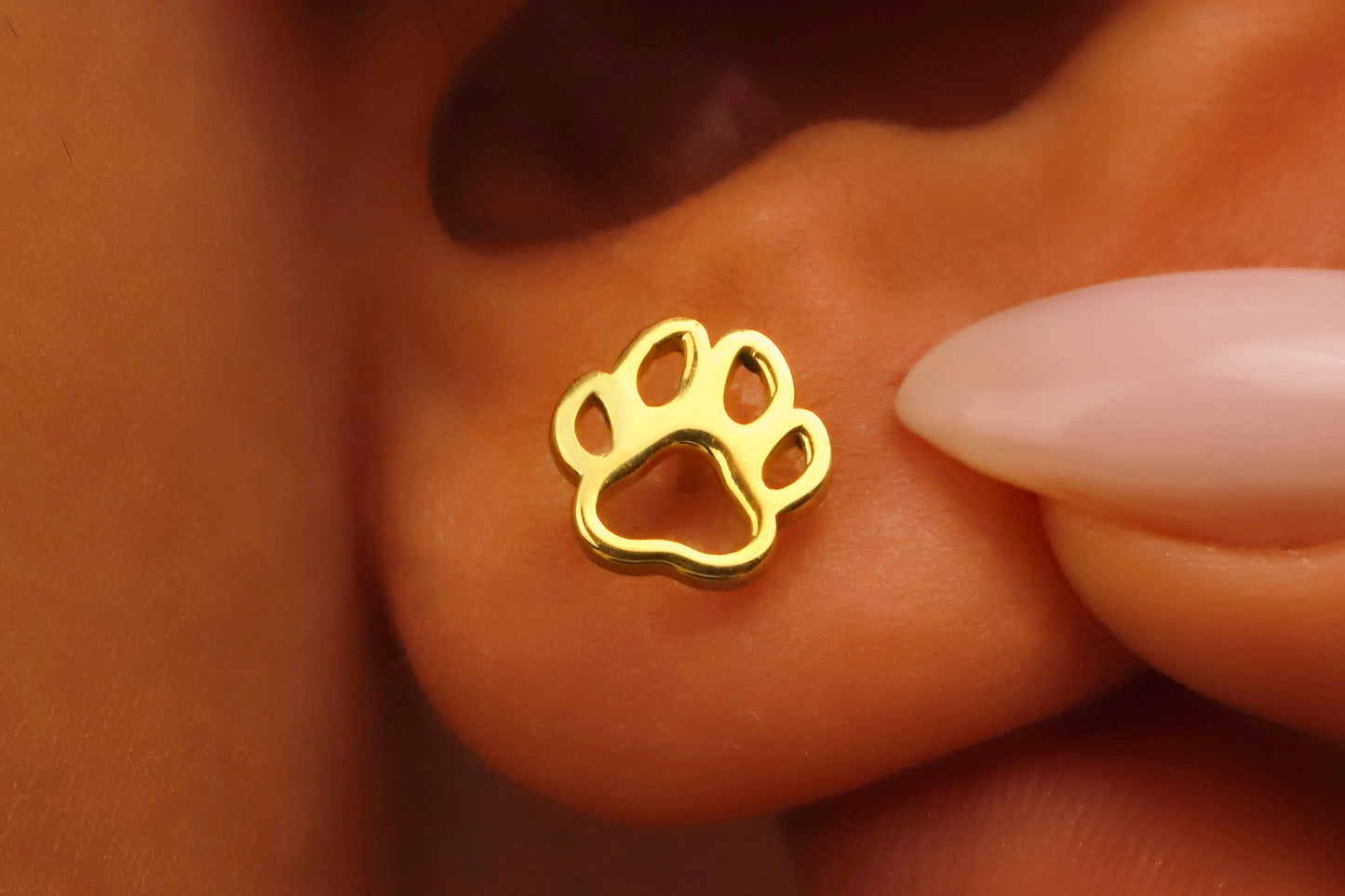 Gold paw print earring being worn on a person's ear.